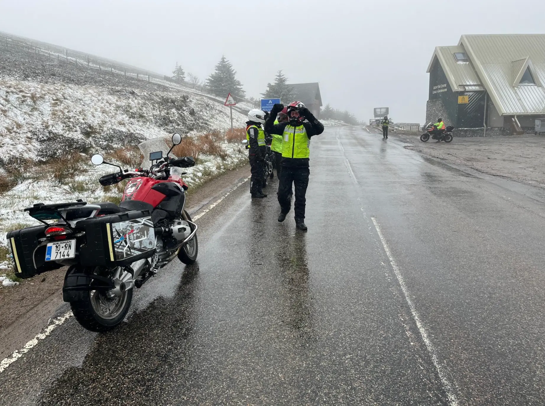 Motorcyclists in high-visibility gear taking a break on a snowy mountain road.