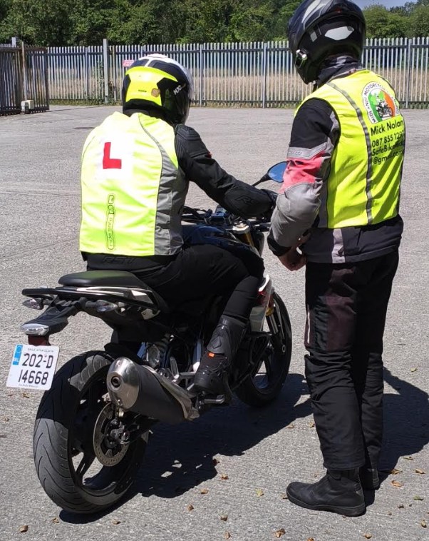 Mick Nolan supervising a learner seated on a motorcycle during a training session.